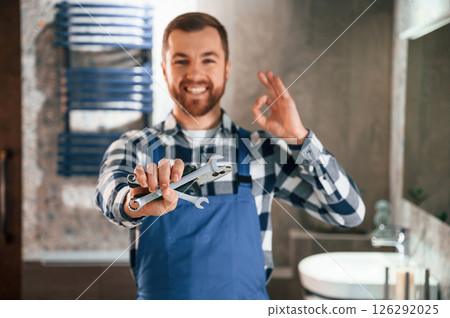 Holding wrenches. Plumber in blue uniform is at work in the bathroom 126292025