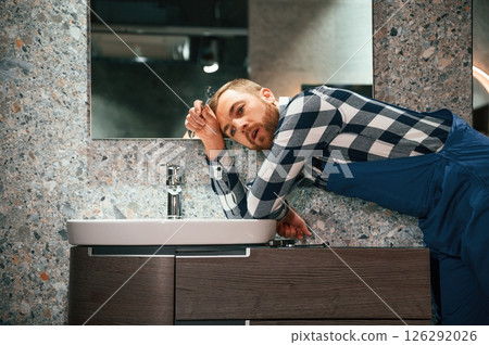 Can't fix the crane. Plumber in blue uniform is at work in the bathroom Can't fix the crane. Plumber in blue uniform is at work in the bathroom 126292026