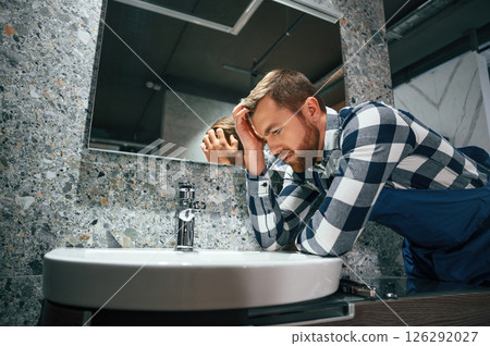 Can't fix the crane. Plumber in blue uniform is at work in the bathroom Can't fix the crane. Plumber in blue uniform is at work in the bathroom 126292027
