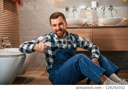 Positive plumber in blue uniform is at work in the bathroom 126292032