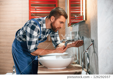 Plumber in blue uniform is at work in the bathroom Plumber in blue uniform is at work in the bathroom 126292037