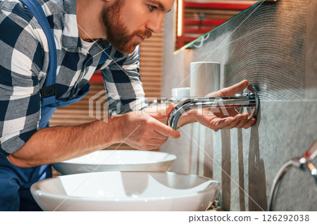 Close up view. Fixing water tap. Plumber in blue uniform is at work in the bathroom 126292038