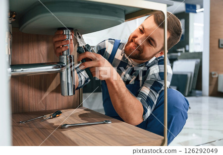 Busy by repairing siphon. Plumber in blue uniform is at work in the bathroom 126292049