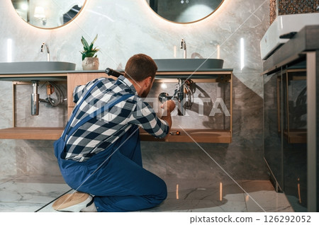 Busy by repairing siphon. Plumber in blue uniform is at work in the bathroom 126292052
