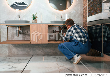 Busy by repairing siphon. Plumber in blue uniform is at work in the bathroom 126292053