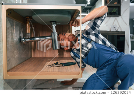 Busy by repairing siphon. Plumber in blue uniform is at work in the bathroom 126292054