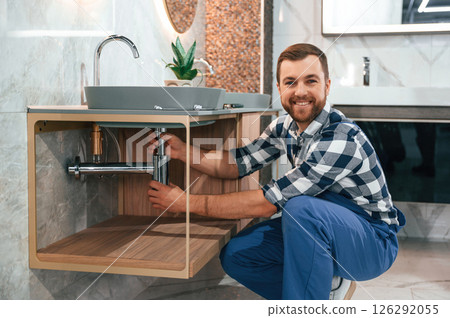 Positive plumber in blue uniform is at work in the bathroom Positive plumber in blue uniform is at work in the bathroom 126292055