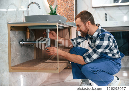 Plumber in blue uniform is at work in the bathroom 126292057