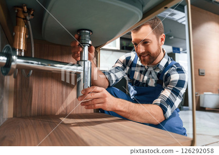 Close up view. Fixing water tap. Plumber in blue uniform is at work in the bathroom Close up view. Fixing water tap. Plumber in blue uniform is at work in the bathroom 126292058