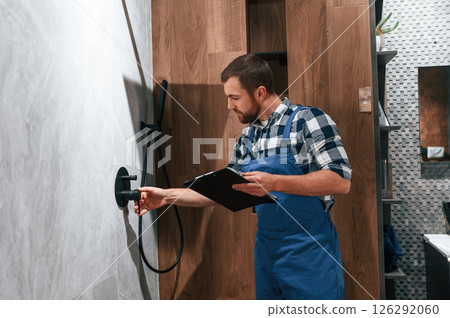Repairs the shower faucet. Plumber in blue uniform is at work in the bathroom 126292060