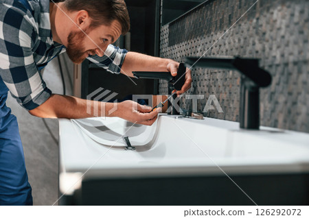 Side view. Fixing water tap. Plumber in blue uniform is at work in the bathroom 126292072