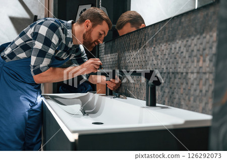 Side view. Fixing water tap. Plumber in blue uniform is at work in the bathroom 126292073