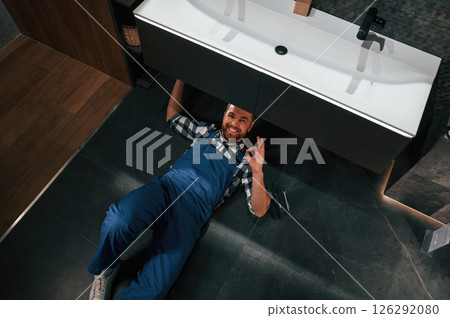 Job is done. Lying down on the floor. Plumber in blue uniform is at work in the bathroom 126292080
