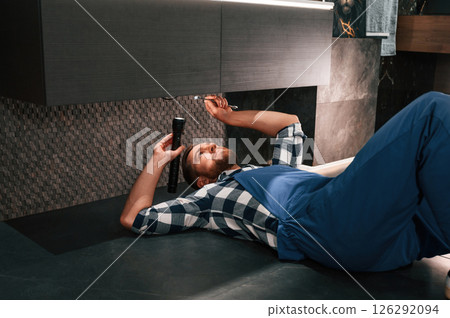 Using flashlight. Fixing water tap. Plumber in blue uniform is at work in the bathroom Using flashlight. Fixing water tap. Plumber in blue uniform is at work in the bathroom 126292094