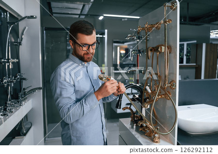 Selects a shower faucet. Man chooses a products in a sanitary ware store 126292112