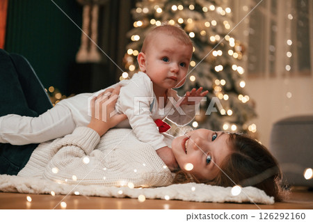 Holding boy in hands. Girl with her little son is at home, celebrating new year Holding boy in hands. Girl with her little son is at home, celebrating new year 126292160