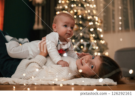 Holding boy in hands. Girl with her little son is at home, celebrating new year Holding boy in hands. Girl with her little son is at home, celebrating new year 126292161
