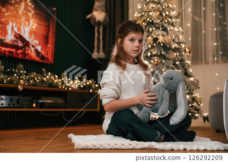 Holding toy in hands. Portrait of little girl that is at home celebrating new year Holding toy in hands. Portrait of little girl that is at home celebrating new year 126292209