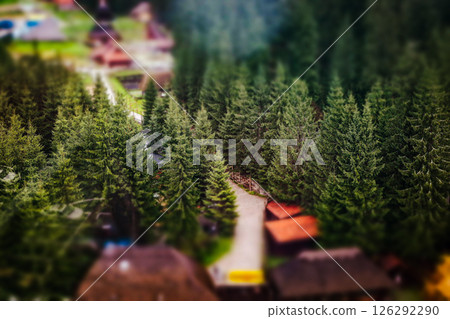 A winding path leads to cabins surrounded by lush green trees in a beautiful mountainous landscape. A high-angle shot showcases picturesque landscape. 126292290