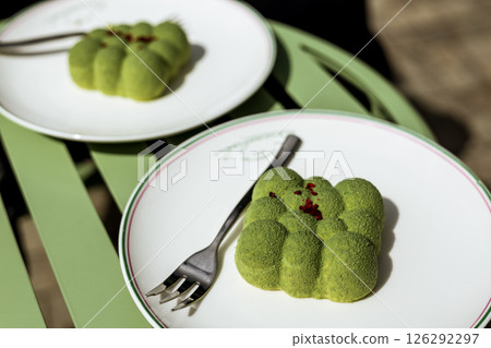 A beautifully presented green desserts sit elegantly on a white plate next to a fork A green-hued dessert rests on a plate under natural light in cafe 126292297