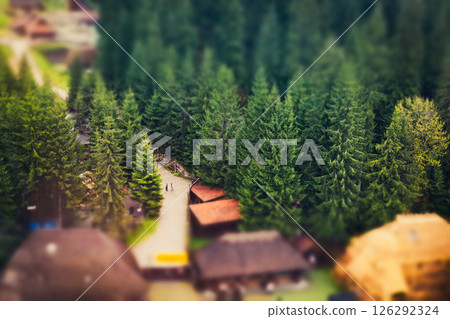 A winding path leads to cabins surrounded by lush green trees in a beautiful mountainous landscape. A high-angle shot showcases picturesque landscape. 126292324