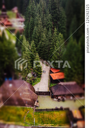 A winding path leads to cabins surrounded by lush green trees in a beautiful mountainous landscape. A high-angle shot showcases picturesque landscape. A winding path leads to cabins surrounded by lush green trees in a beautiful mountainous landscape. A high-angle shot showcases picturesque landscape. 126292325