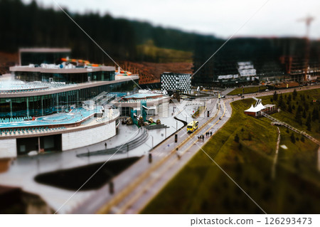 A modern resort and spa complex with swimming pools and a water slide, nestled in a natural setting surrounded by trees. A glass facade exterior. A modern resort and spa complex with swimming pools and a water slide, nestled in a natural setting surrounded by trees. A glass facade exterior. 126293473