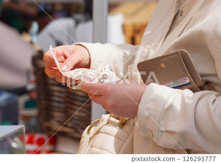 A Woman Counting Cash at Market with Wallet and Beige Purse 126293777