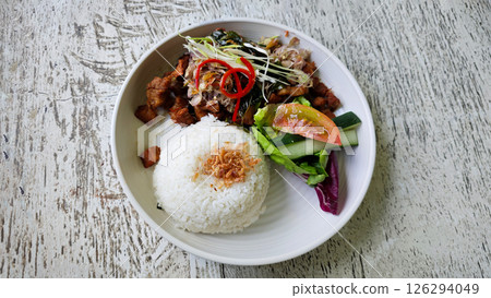 Crispy Fried Pork with Steamed Rice and Fresh Sambal Matah, Served with Salad Garnish on a Rustic Wooden Table 126294049