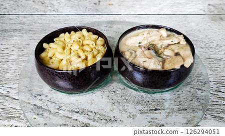 Two Ceramic Bowls with Macaroni Pasta and Creamy Mushroom Chicken on Glass Plate with Rustic Wooden Background Two Ceramic Bowls with Macaroni Pasta and Creamy Mushroom Chicken on Glass Plate with Rustic Wooden Background 126294051