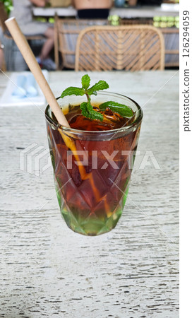Refreshing Iced Black Tea with Mint Garnish in Textured Glass on Rustic Wooden Table at an Outdoor Cafe Setting 126294059