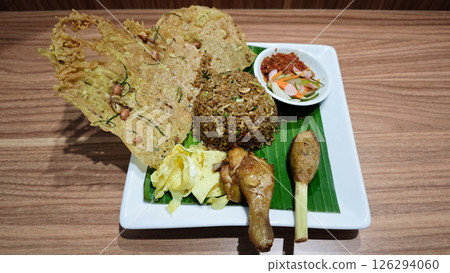 Traditional Indonesian Fried Rice with Sambal and Crispy Peanut Crackers on Banana Leaf Plating with Grilled Chicken Drumstick and Sate Lilit Garnished on White Square Plate Traditional Indonesian Fried Rice with Sambal and Crispy Peanut Crackers on Banana Leaf Plating with Grilled Chicken Drumstick and Sate Lilit Garnished on White Square Plate 126294060