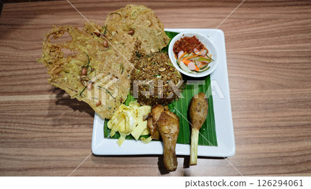 Traditional Indonesian Fried Rice with Sambal and Crispy Peanut Crackers on Banana Leaf Plating with Grilled Chicken Drumstick and Sate Lilit Garnished on White Square Plate Traditional Indonesian Fried Rice with Sambal and Crispy Peanut Crackers on Banana Leaf Plating with Grilled Chicken Drumstick and Sate Lilit Garnished on White Square Plate 126294061