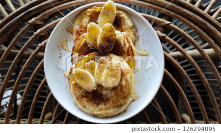 Delicious Banana Pancakes Topped with Sliced Bananas and Drizzled Honey on a White Plate in a Rustic Setting 126294095