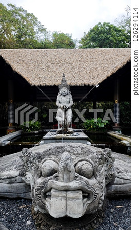 Traditional Balinese Water Fountain Statue with Stone Carvings and Thatch Roof Pavilion Surrounded by Greenery in Tropical Garden Setting Traditional Balinese Water Fountain Statue with Stone Carvings and Thatch Roof Pavilion Surrounded by Greenery in Tropical Garden Setting 126294114
