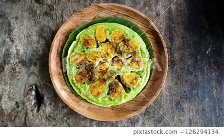 Vibrant green banana pancake with caramelized banana slices and brown sugar, served on a wooden plate with a rustic dark wood background 126294134