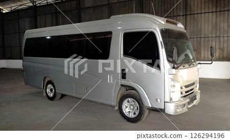 Silver Minibus Parked Indoors in a Warehouse with Dim Lighting, Capturing the Exterior Profile of a Modern Passenger Vehicle in a Spacious Industrial Setting 126294196
