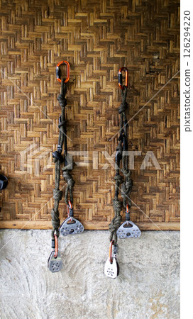 Outdoor climbing equipment with carabiners and rope hanging on bamboo wall in a rustic setting showcasing adventure tools and safety gear 126294220