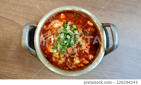 Close-up of Sundubu Jjigae Korean Soft Tofu Stew with Green Onion Garnish in a Traditional Brass Pot on a Wooden Table Close-up of Sundubu Jjigae Korean Soft Tofu Stew with Green Onion Garnish in a Traditional Brass Pot on a Wooden Table 126294243
