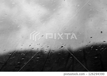 Raindrops on a window, blurred background, an atmospheric monochrome scene. Water droplets on a glass with rain streaks in cold season. Rainy weather. 126294390