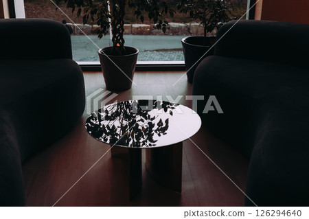 Stylish indoor space featuring two armchairs, a round table, indoor plants near a window. A modern interior setting with armchairs, a reflective table 126294640