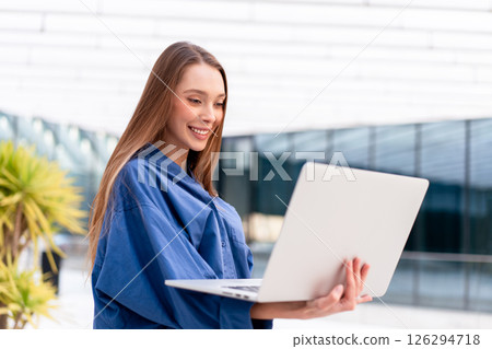 Smiling businesswoman in blue shirt using laptop Smiling businesswoman in blue shirt using laptop 126294718