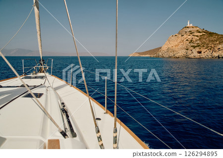 view from a sailing boat to an island with a lighthouse in clear sunny weather, the bow of the boat, the shrouds of the yacht, reflection on the water, mountains in the background view from a sailing boat to an island with a lighthouse in clear sunny weather, the bow of the boat, the shrouds of the yacht, reflection on the water, mountains in the background 126294895