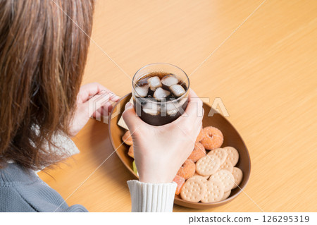 A woman drinking cola while eating a platter of sweets for a snack 126295319