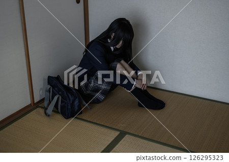 一名高中女生盤腿坐在日式房間的角落。霸凌、拒絕上學、社交退縮、對未來感到焦慮 126295323