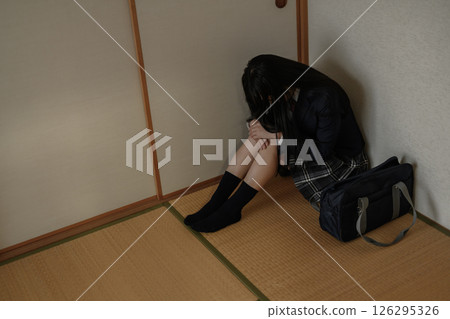 High school girl sitting cross-legged in the corner of a Japanese-style room. Bullying, school refusal, social withdrawal, anxiety about the future. Natural color. High school girl sitting cross-legged in the corner of a Japanese-style room. Bullying, school refusal, social withdrawal, anxiety about the future. Natural color. 126295326