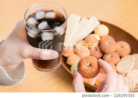 Hands of a woman eating a plate of sweets while drinking cola 126295383