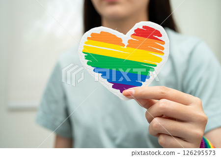 Asian lady wearing rainbow flag wristbands and hold red heart, symbol of LGBT pride month celebrate annual in June social of gay, lesbian, bisexual, transgender, human rights. Asian lady wearing rainbow flag wristbands and hold red heart, symbol of LGBT pride month celebrate annual in June social of gay, lesbian, bisexual, transgender, human rights. 126295573