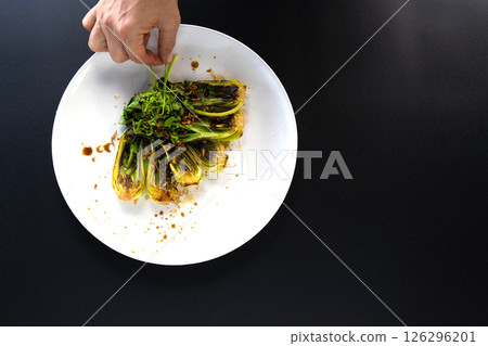 Hand is garnishing bok choy with spices in an Asian kitchen, showcasing preparation. 126296201