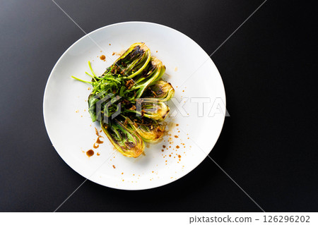 Fresh bok choy artfully arranged on a white plate, flaunting vibrant green leaves and sauce. 126296202